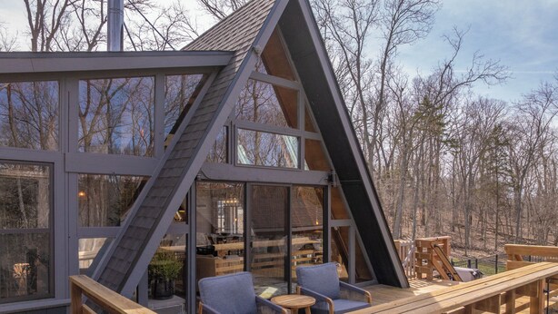 A wooden deck with outdoor seating, a glass-enclosed room, and a view of the surrounding trees. - Chalet Harmonie by Innsbrook Vacations! (Innsbrook)