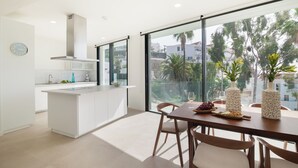 A modern kitchen with a large island, a dining area with a table and chairs, and a view through large windows. - Lux 200m NEW D Villa with heated pool, ocean view (Costa Adeje)