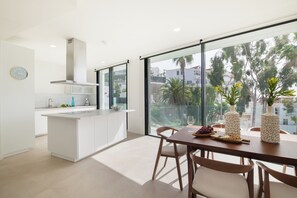 Eine moderne Küche mit einer großen Kochinsel, einem Essbereich mit Tisch und Stühlen sowie Blick durch große Fenster.