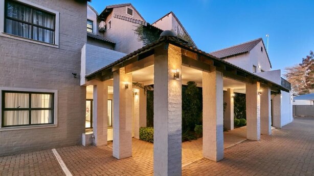 A building with a covered outdoor area supported by columns, a paved entrance, and a brick pathway. - Golden Crystal Hotel (Gaborone)
