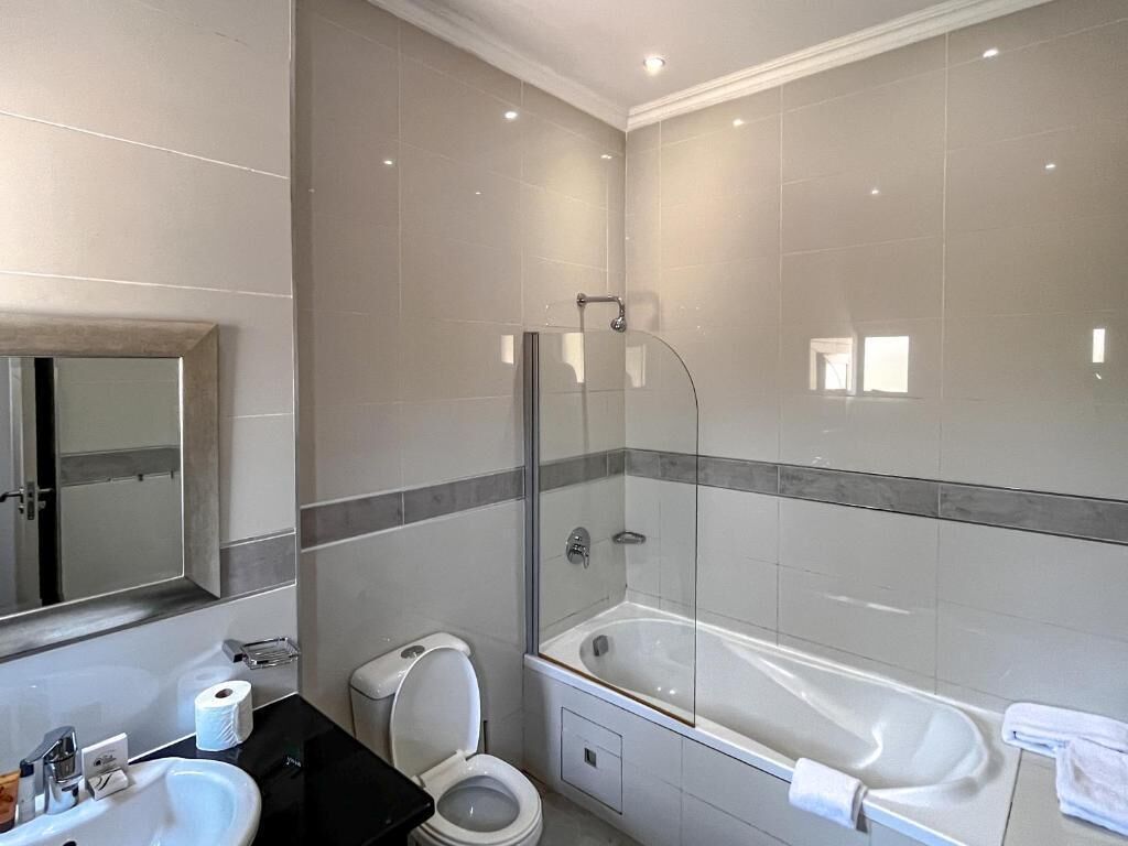 A modern bathroom with a glass-enclosed shower, a bathtub, a toilet, and a sink.