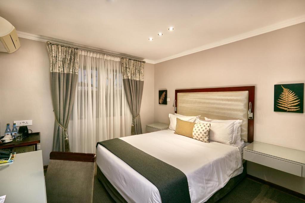 Una habitación de hotel con cama, escritorio, silla, mesita de noche y ventana con cortinas.