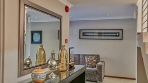 A modern living room with a large mirror, a sofa, and decorative items on a console table. - Golden Crystal Hotel (Gaborone)