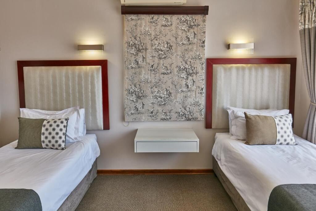 A hotel room with two beds, a wall-mounted artwork, and a small white shelf.
