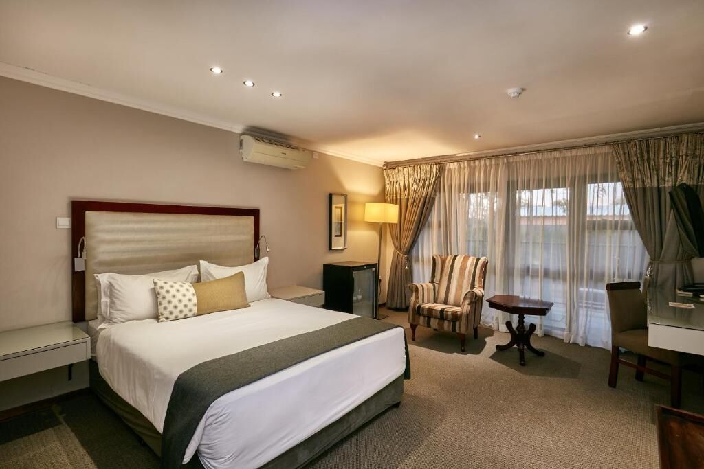 A hotel room with a large bed, a desk, a chair, a lamp, and a window with curtains.