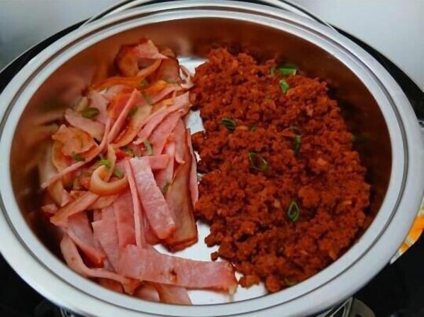 Une assiette en acier inoxydable garnie de tranches de jambon et d’une portion de viande rouge, probablement du bœuf ou du porc.