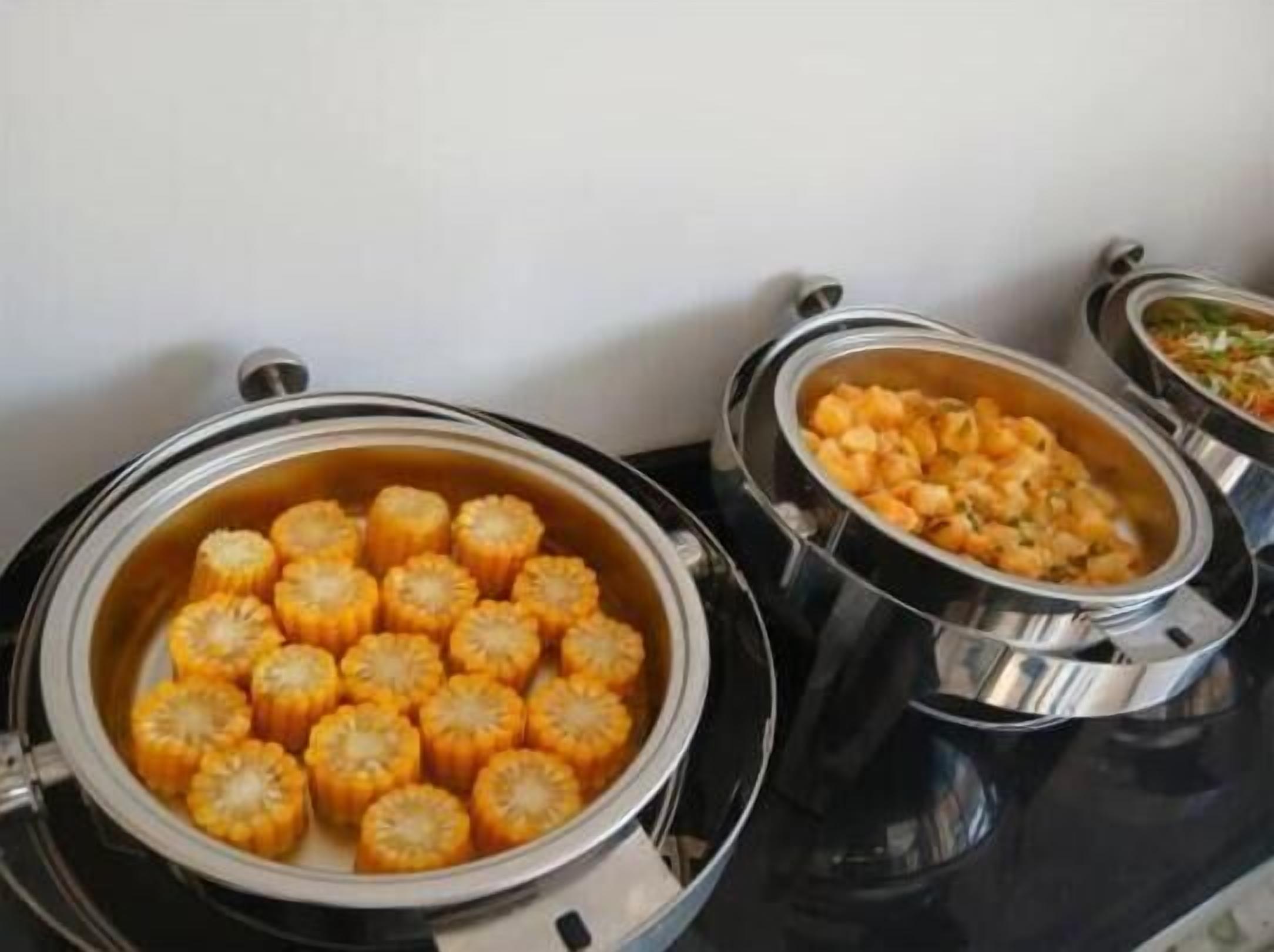 Un coin cuisine avec des ustensiles de cuisine en acier inoxydable sur une cuisinière, notamment des casseroles contenant des épis de maïs et une autre contenant un plat ressemblant à un ragoût.