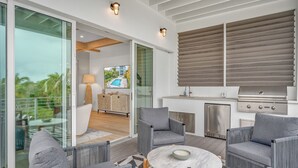 Un espacio exterior moderno con comedor, cocina y puertas correderas que dan a una zona de piscina.
