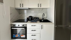 A modern kitchen with white cabinets, a stainless steel refrigerator, a built-in oven, and a sink with a faucet. - Loutraki s Hideaway in Loutraki (Loutraki-Agioi Theodoroi)