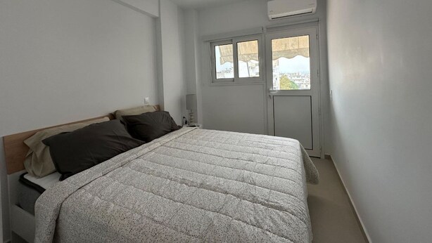 A bedroom with a bed, a window, an air conditioning unit, and a wall-mounted TV. - Loutraki s Hideaway in Loutraki (Loutraki-Agioi Theodoroi)