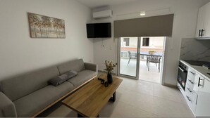 A living room with a sofa, a coffee table, a TV, and a sliding glass door leading to a balcony. - Loutraki s Hideaway in Loutraki (Loutraki-Agioi Theodoroi)