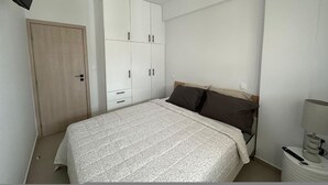 A bedroom with a bed, a wardrobe, a door, and a bedside table with a lamp. - Loutraki s Hideaway in Loutraki (Loutraki-Agioi Theodoroi)