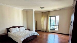 A bedroom with a large bed, a wardrobe, and a window with curtains. - Luxury Oasis: 2-bedroom apartment w/ downtown city views (Addis Ababa)
