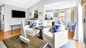A modern living room with a flat-screen TV, a sailboat model, and a dining area with a table and chairs. - Family Friendly Pensacola Home Near Gulf Breeze (Pensacola)