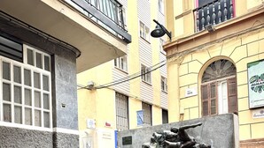 A public square with a central sculpture of a climbing figure, surrounded by stone steps and buildings with balconies and windows. - Suitehomes Penthouse Granados (Málaga)