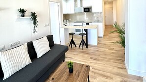 A modern living room with a sofa, a coffee table with a plant, a kitchen area with white cabinets, and a wooden floor. - Suitehomes Penthouse Granados (Málaga)