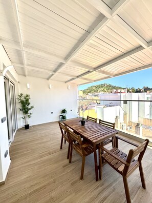 A spacious balcony with a wooden table and chairs, potted plants, and a view of the cityscape. - Suitehomes Penthouse Granados (Málaga)