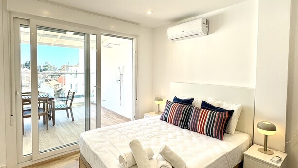 A hotel room with a bed, a nightstand, a lamp, a sliding glass door leading to an outdoor area with a table and chairs. - Suitehomes Penthouse Granados (Málaga)
