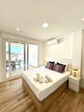 A hotel room with a bed, a nightstand, a lamp, a sliding glass door leading to an outdoor area with a table and chairs. - Suitehomes Penthouse Granados (Málaga)