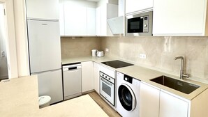 A modern kitchen with white cabinetry, a built-in oven, microwave, and washing machine. - Suitehomes Penthouse Granados (Málaga)