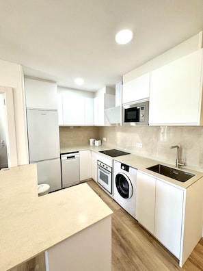 A modern kitchen with white cabinetry, a built-in oven, microwave, and washing machine. - Suitehomes Penthouse Granados (Málaga)