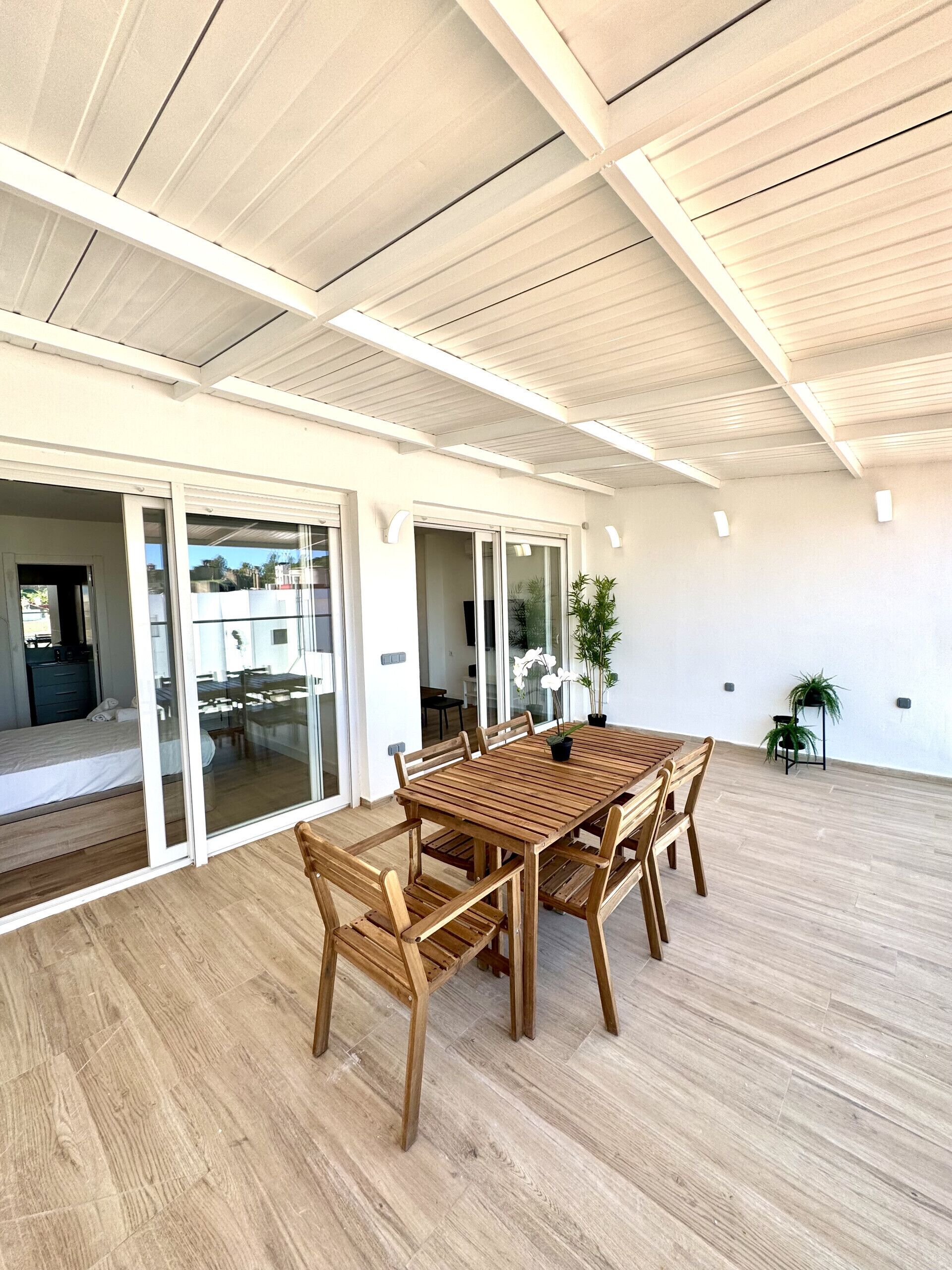 A spacious room with a wooden dining table and chairs, a sliding glass door leading to a balcony, and a ceiling with exposed beams.