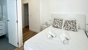 A hotel room with a bed, white bedding, two patterned pillows, a bedside table with a lamp, and an air conditioning unit on the wall. - Suitehomes Penthouse Granados (Málaga)