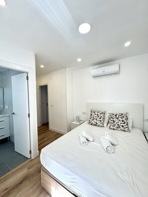 A hotel room with a bed, white bedding, two patterned pillows, a bedside table with a lamp, and an air conditioning unit on the wall. - Suitehomes Penthouse Granados (Málaga)