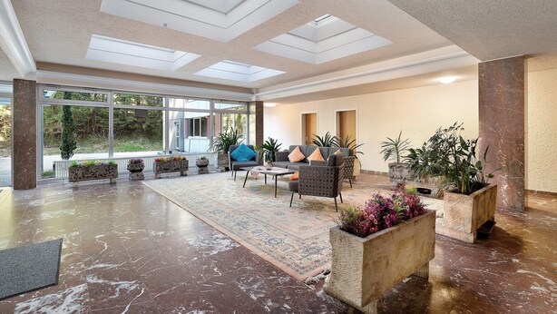 A spacious lobby with a high ceiling, skylights, a patterned rug, seating area with cushions, and potted plants. - Apartment “Forest Elegance” with Mountain View, Balcony and Wi-Fi (Freudenstadt)