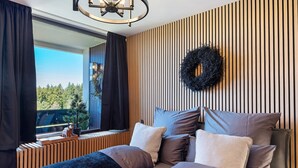 A modern bedroom with a large bed, a window with curtains, a wooden slat wall, and a wreath decoration. - Apartment “Forest Elegance” with Mountain View, Balcony and Wi-Fi (Freudenstadt)