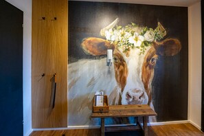 Ein Zimmer mit einer großen Wandmalerei von einer Kuh, einer Holzkabine und einem kleinen Holztisch mit einer Schachtel darauf.