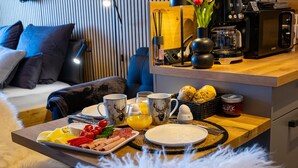 A breakfast tray with eggs, sausages, and fruit on a wooden table in a modern hotel room. - Apartment “Forest Elegance” with Mountain View, Balcony and Wi-Fi (Freudenstadt)