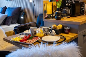 Ein Frühstückswagen mit Eiern, Würstchen und Obst auf einem Holztisch in einem modernen Hotelzimmer.