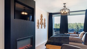 A modern bedroom with a fireplace, a bed with a view, and a chandelier. - Apartment “Forest Elegance” with Mountain View, Balcony and Wi-Fi (Freudenstadt)
