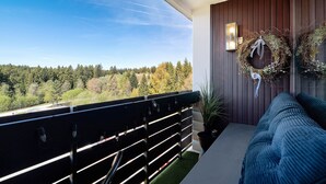 A balcony with a view of a forest, a wooden wall, and a blue sofa. - Apartment “Forest Elegance” with Mountain View, Balcony and Wi-Fi (Freudenstadt)