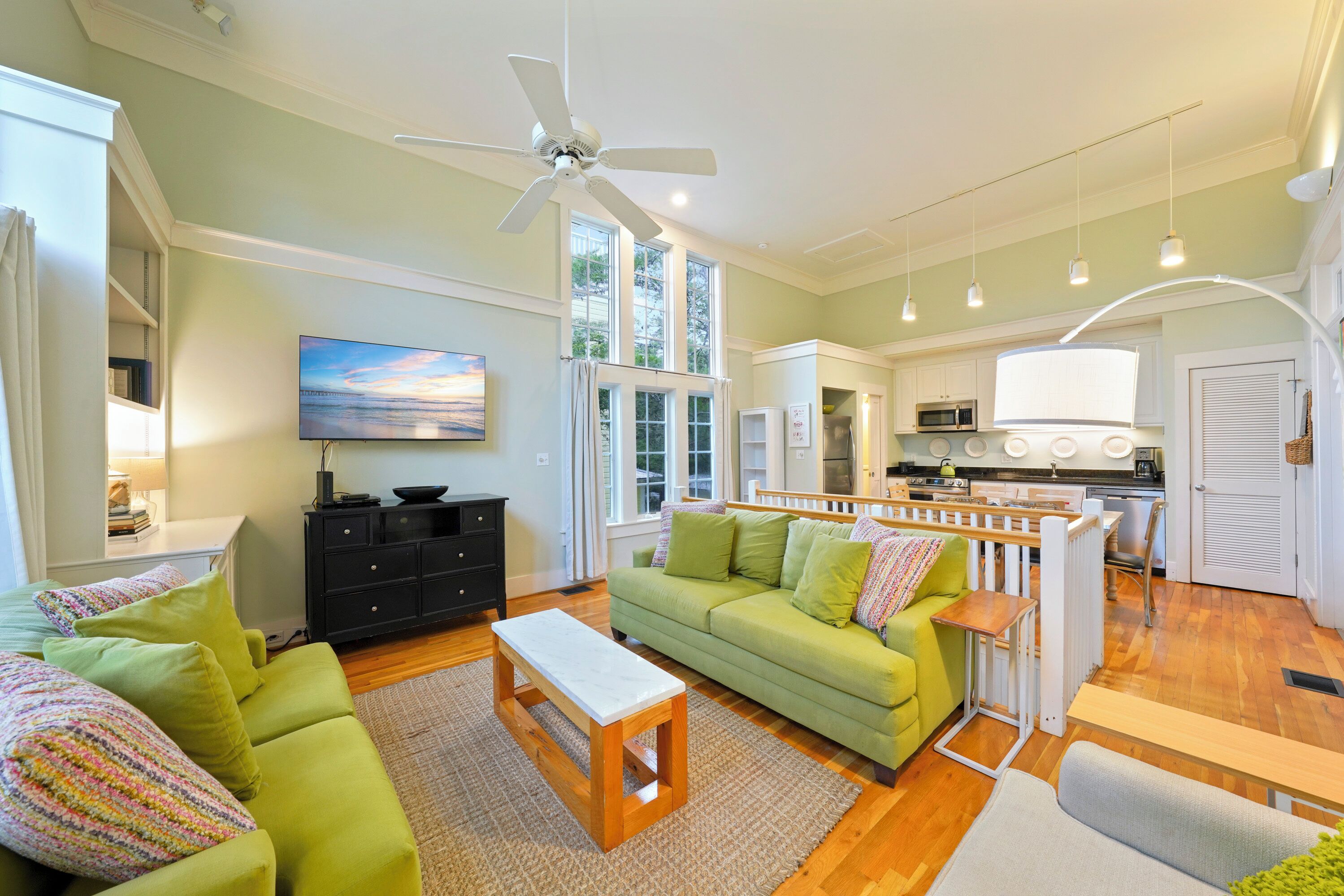 A living room with a green sofa, a white coffee table, a TV, and a kitchen in the background.