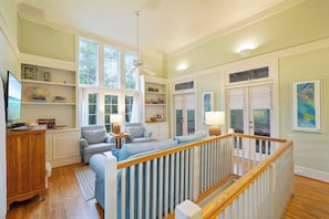 Un salon spacieux avec un plafond haut, de grandes fenêtres, un ventilateur de plafond et une vue sur l’extérieur.