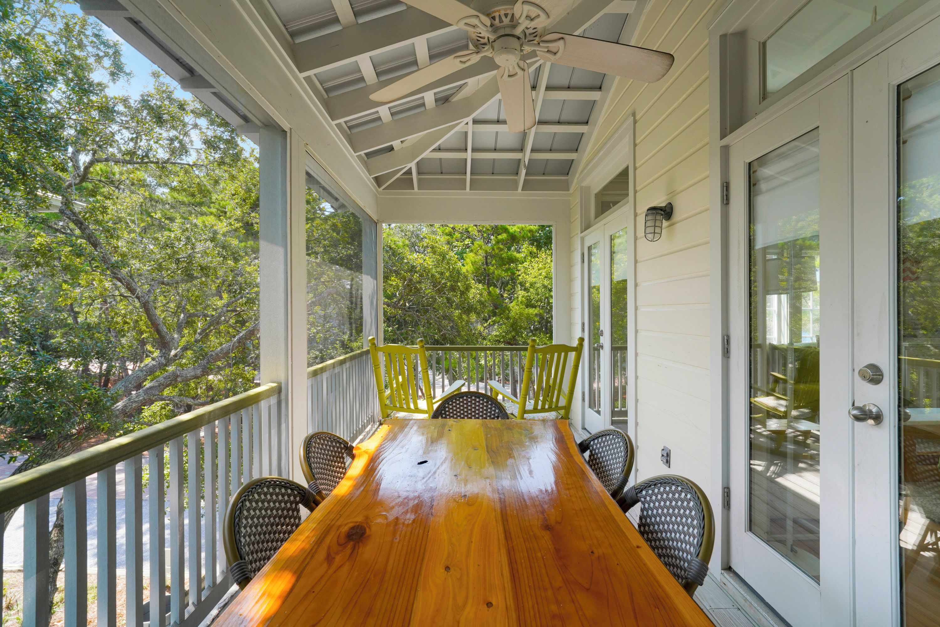 Eine überdachte Veranda mit Holztisch, Stühlen und Deckenventilator.