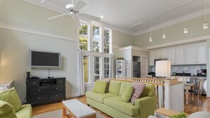 A modern living room with a green sofa, a wooden coffee table, a TV, and a ceiling fan. - Ideal Family Home Prime Location in SeasideFL, 5 Mins to Beach! - +2 Bikes (Santa Rosa Beach)