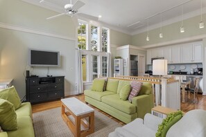 Ein modernes Wohnzimmer mit einem grünen Sofa, einem Holztisch, einem Fernseher und einem Deckenventilator.