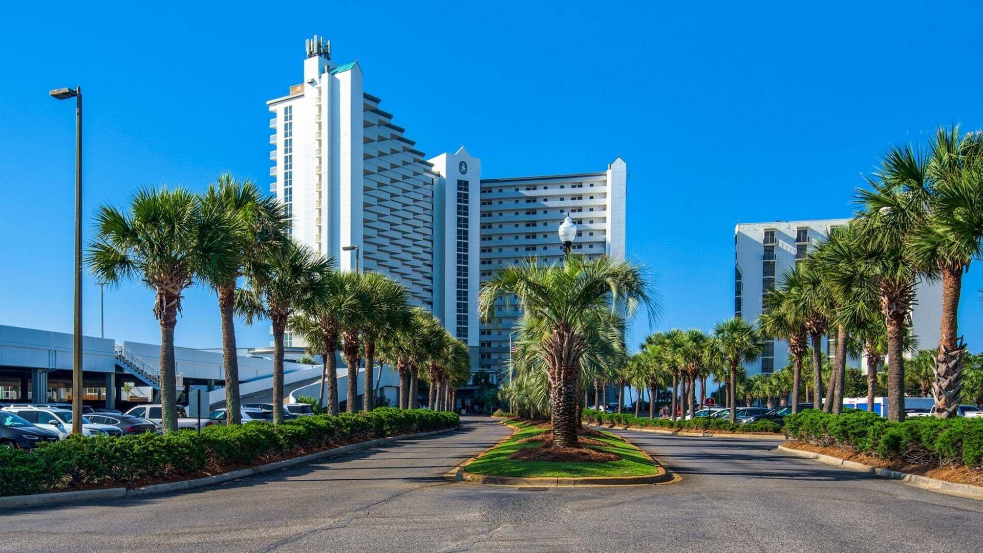 A hotel with a modern design, featuring a central courtyard with palm trees and a clear blue sky.