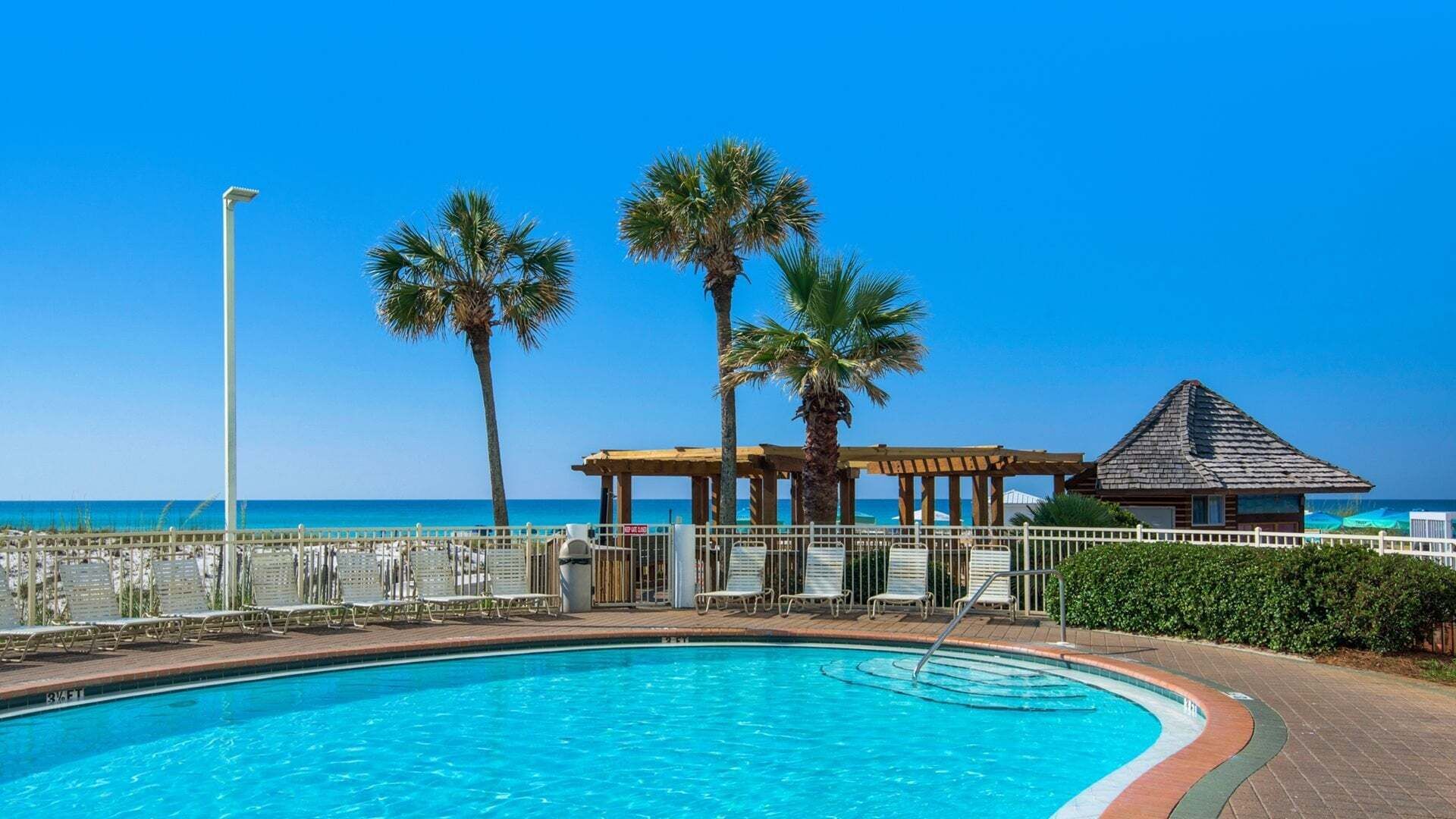 A swimming pool with a wooden deck, palm trees, and a beach view.