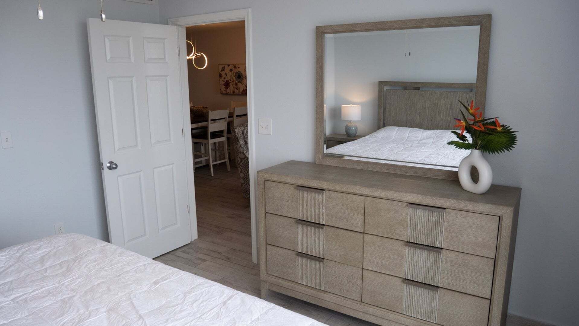 A bedroom with a bed, a dresser, a mirror, and a door leading to another room.