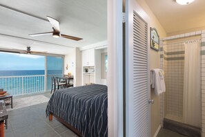 Ein Zimmer mit Bett, Deckenventilator, Meerblick, Badezimmer mit Dusche und Balkon mit Tisch und Stühlen.