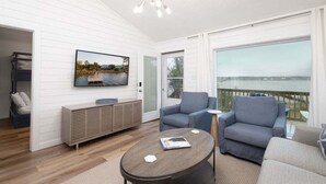 A modern living room with a TV, sofas, a coffee table, and a view of the water. - Sailhouse West 2 Bedroom Duplex (Gulf Shores)