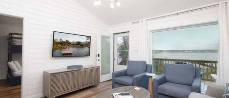 Een moderne woonkamer met een televisie, banken, een salontafel en uitzicht op het water.