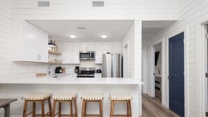 A kitchen with white cabinetry, a central island with stools, a microwave, and a refrigerator. - Sailhouse West 2 Bedroom Duplex (Gulf Shores)