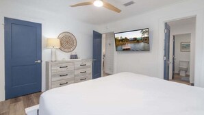 A bedroom with a bed, a ceiling fan, a TV, a dresser, and a door leading to a bathroom. - Sailhouse West 2 Bedroom Duplex (Gulf Shores)