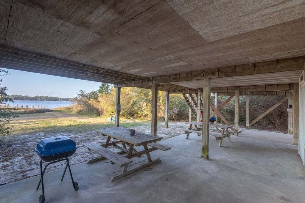 Ein überdachter Picknickbereich im Freien mit Picknicktischen und Grill, mit Blick auf ein Gewässer und eine natürliche Landschaft.
