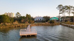A wooden dock extending into a body of water with buildings and trees in the background. - Sailhouse West 2 Bedroom Duplex (Gulf Shores)